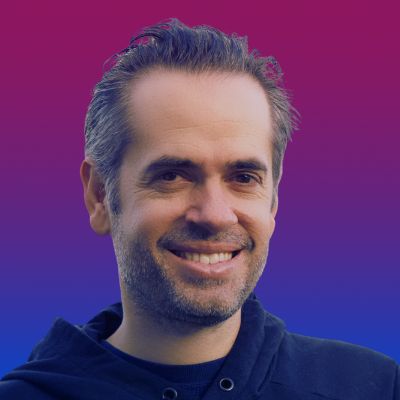 Man smiling in hoodie against pink to blue gradient background. Casual and professional look.